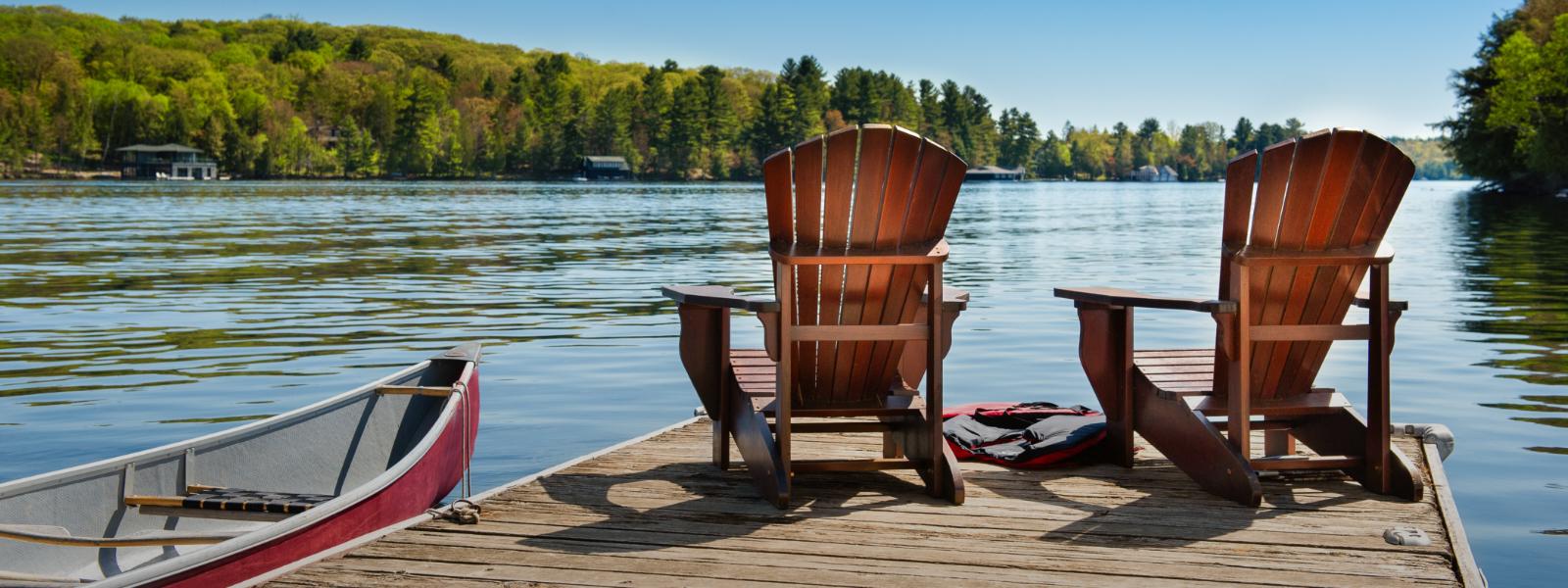 Two wooden chairs overlooking a lake on a sunny day. 