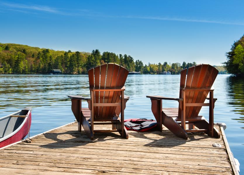 Two wooden chairs overlooking a lake on a sunny day. 