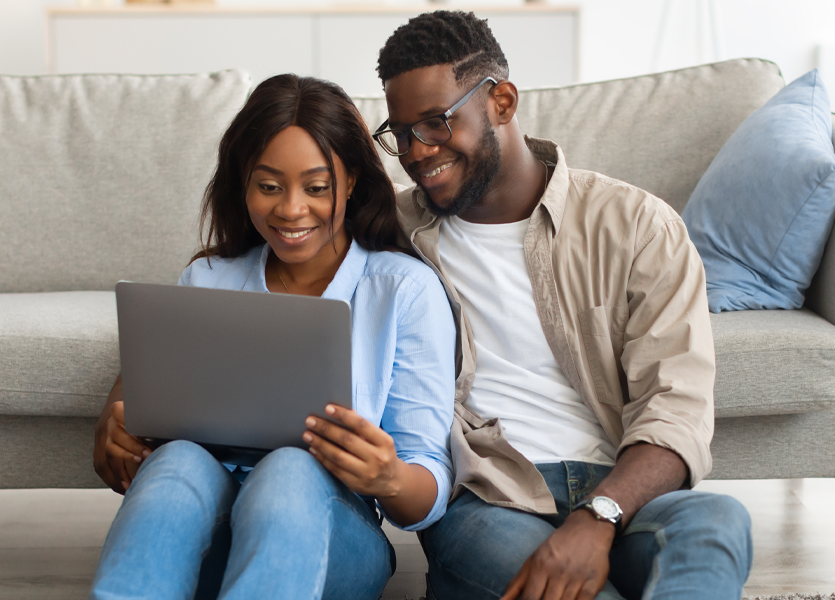 A couple in their living room, browsing a laptop while smiling. 