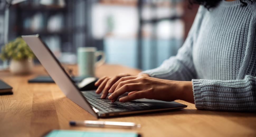 Self-guided upgrade - Woman wearing a blue sweater, sitting at a desk, working on a laptop computer