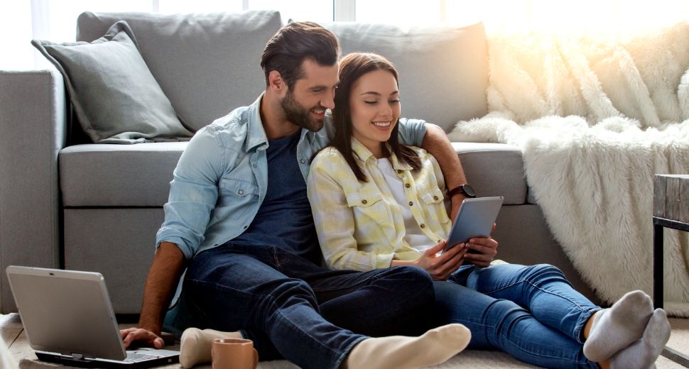 Couple sitting on floor infront of the couch looking at a tablet