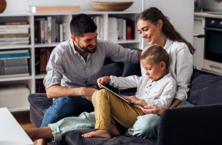 Family of three sitting on couch and looking at an ipad