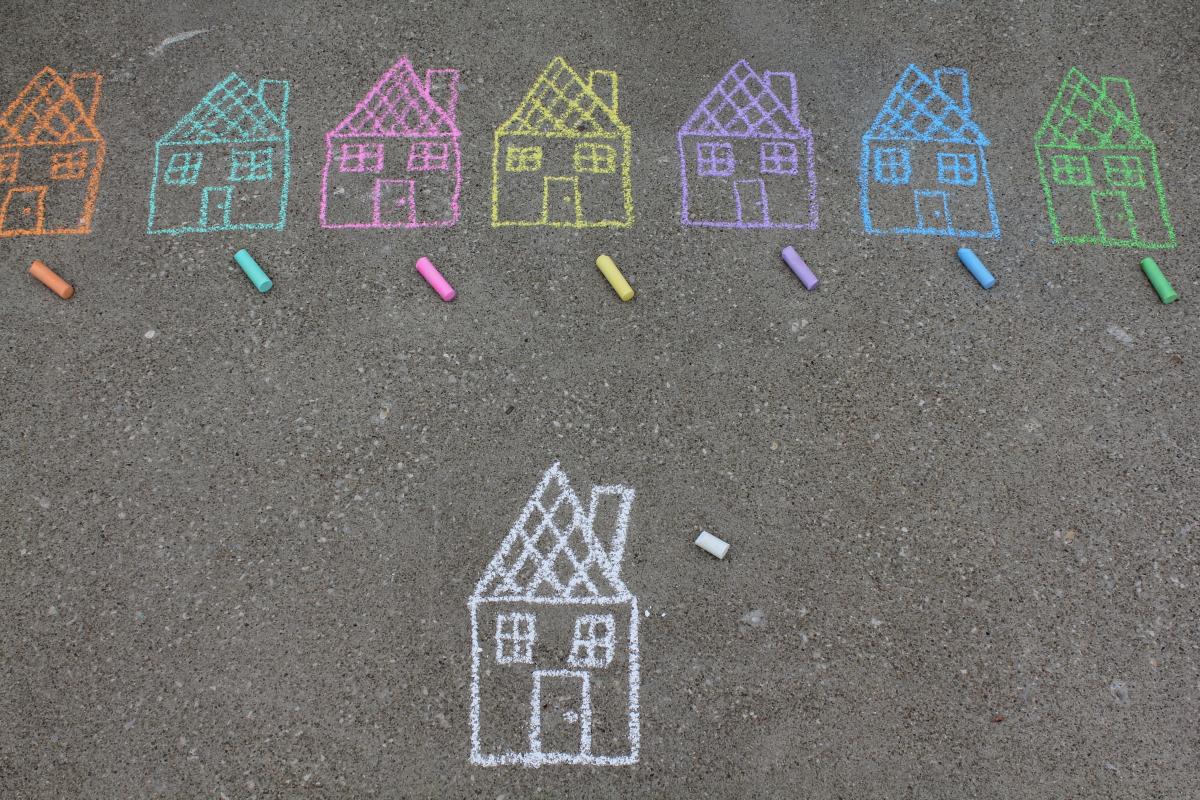 A row of colorful chalk houses, drawn on pavement. Below, there is a single house drawn in white chalk. 