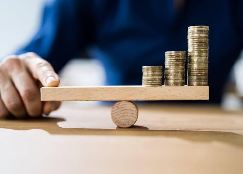 A scale that balances coins on one side and a person's hand holding down the other side. 