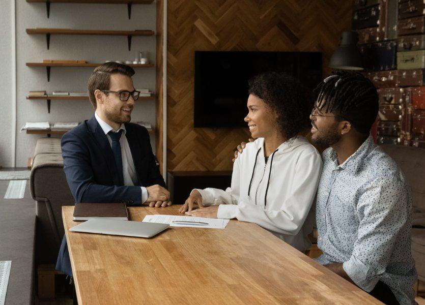 An agent and two clients, seated at a table. The agent and one client are shaking hands. 